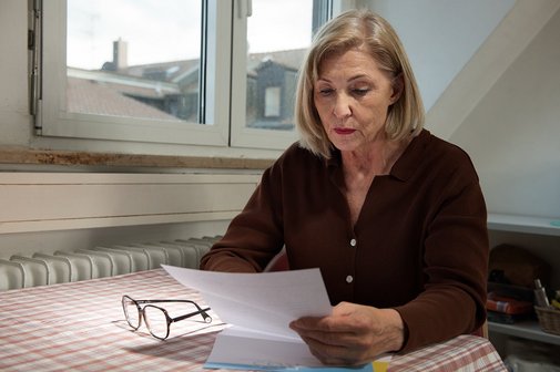 Besorgte Seniorin liest Schreiben Eine ältere Frau sitzt an einem Küchentisch und liest einen Brief, sie sieht ernst und besorgt aus.